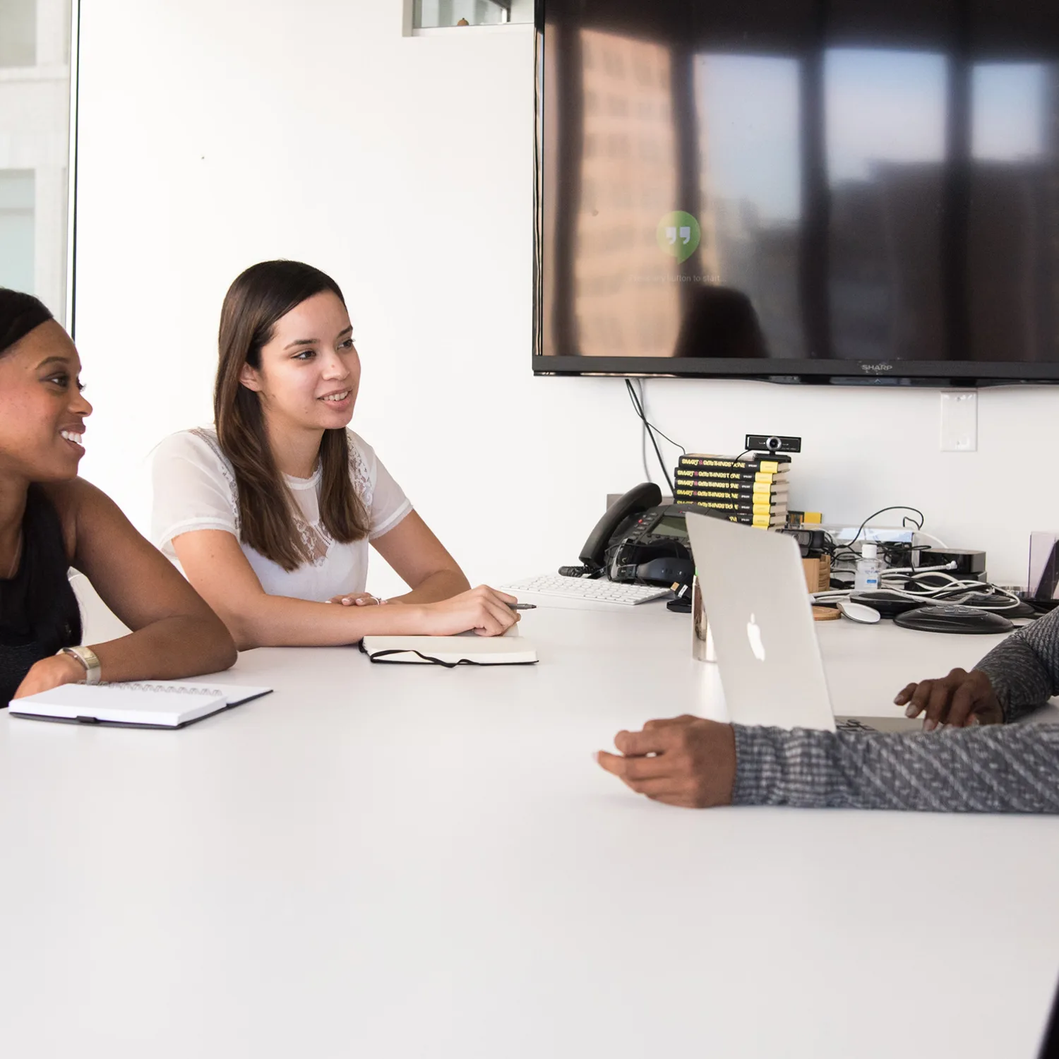 Two women sitting at a table in an office meeting room, opposite to a third woman who has a laptop