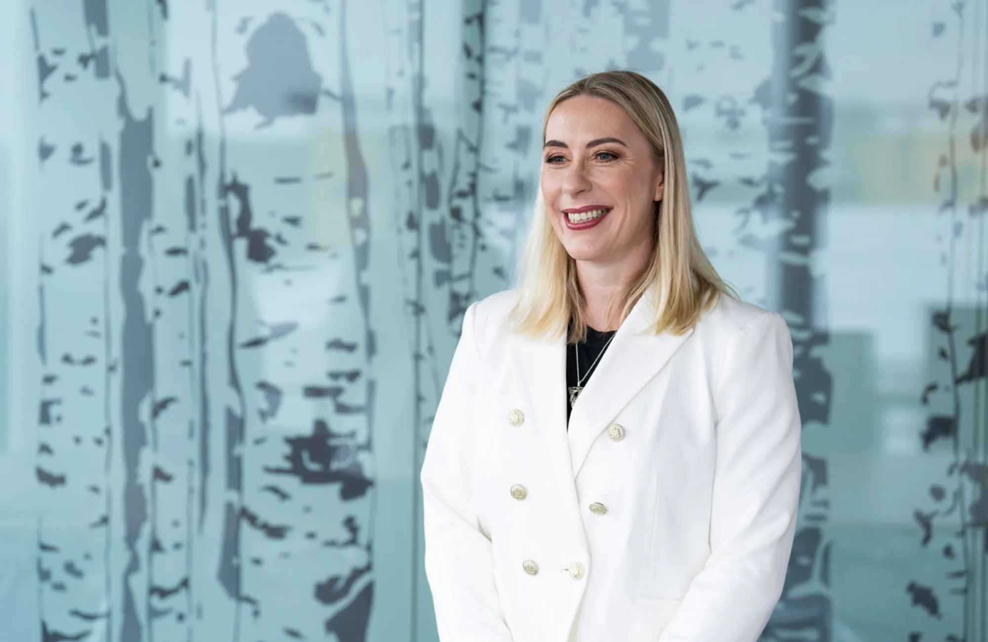 Carole looking away from camera and smiling in a white double breasted jacket