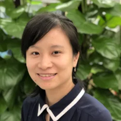 Annie in a navy blue top with a white trim on her collar in front of a green bush